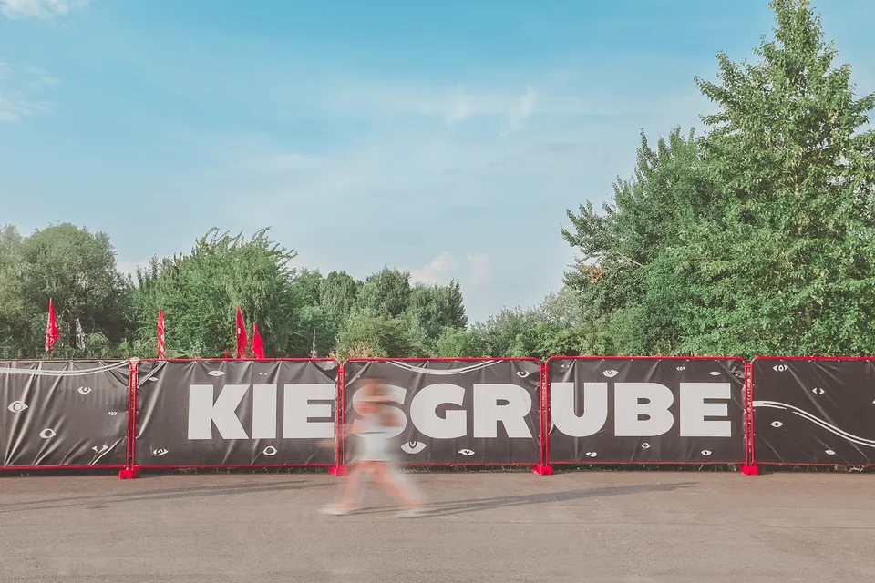 Kiesgrube Open Air, Event und Struktur: Festivaleingang mit der Schrift „Kiesgrube“ auf einem Bauzaun unter blauem Himmel