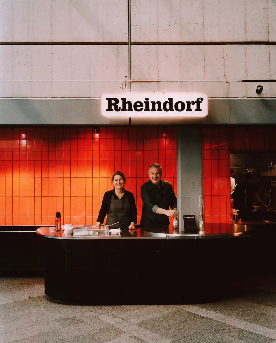 Luminaden, brand space: counter with a sign “Rheindorf” and two staff in front of red tiles