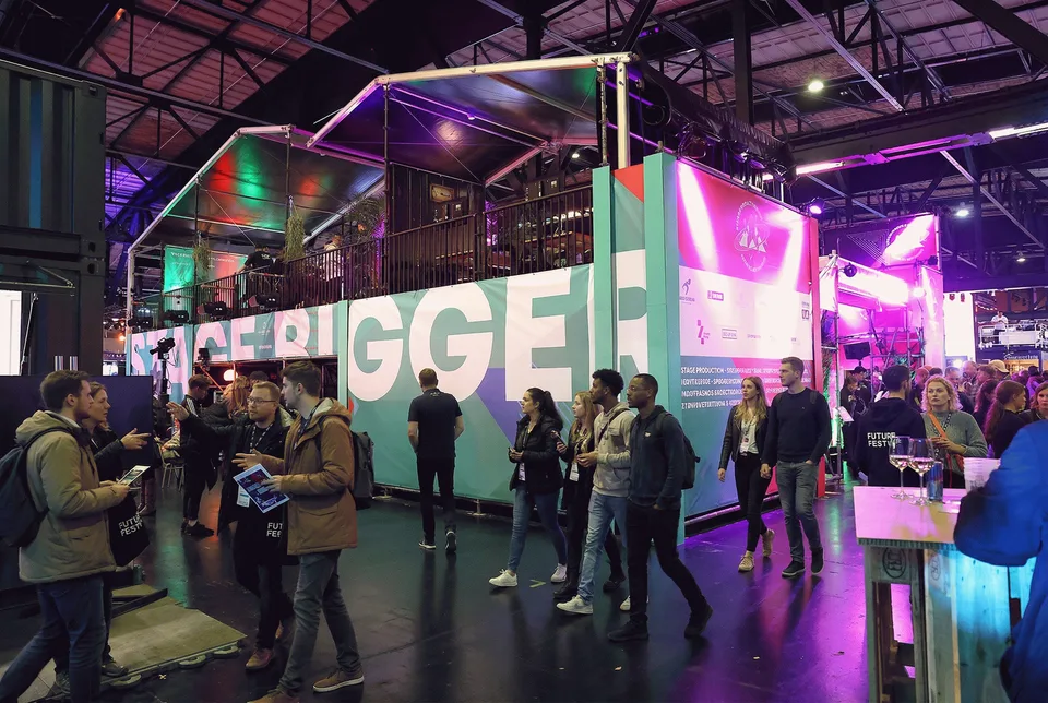 Stageventure & Friends, Event und Struktur: Besucher:innen vor der beleuchteten Wand „Stage Bigger“ in violettem Licht